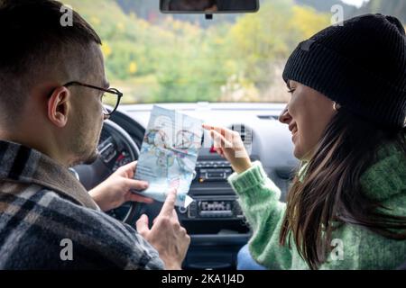 A man and lady holding and looking at paper map, sitting inside car. Stock Photo