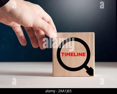 Male hand places the wooden cubes with the word timeline in a magnifying glass. Timeline and project analysis concept. Stock Photo