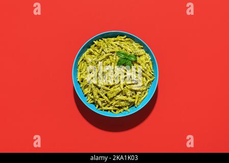 Trofie al Pesto, a delicious Italian dish minimalist on a red-colored table. Short pasta called Trofie with pesto sauce and parmesan. Stock Photo