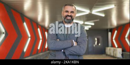A gray-haired fifty-year-old man businessman in an underground parking lot stands with his arms folded across his chest Stock Photo