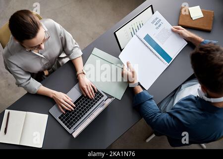 Above shot of two young economists sitting by workplace in front of laptops and working with financial information and documents Stock Photo