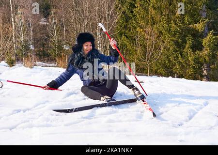 Laughing cheerful young girl fell down while skiing in the forest Stock Photo
