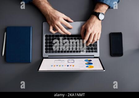 Above shot of hands of young businessman over laptop keyboard and touchpad during analysis of financial diagrams and chart Stock Photo