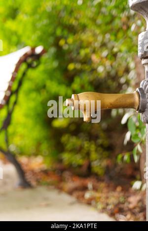 Elegant urban public drinking fountain with a wet shiny tap in a natural park. Valve with water drops. Scenic view Stock Photo