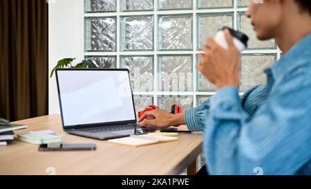 rear view, Professional millennial Asian male office worker or web engineer working on his project on laptop while sipping coffee at his desk. Stock Photo