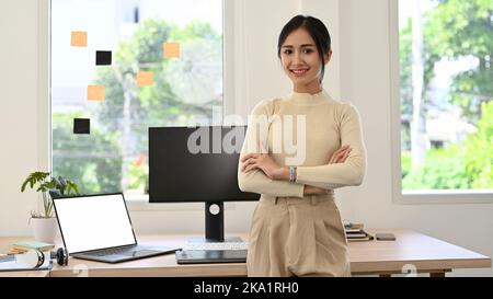 Attractive and beautiful millennial Asian businesswoman or female CEO in casual clothes arms crosses, smiling, looking at camera  while standing in he Stock Photo