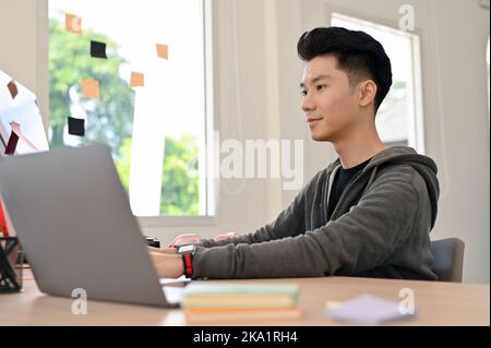 Handsome young Asian male programmer or web developer in casual clothes working at his desk. Stock Photo