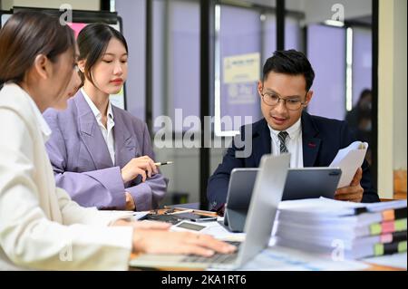 Smart millennial Asian businessman or male financial analyst explaining and sharing his ideas to his team while working together in the office. Stock Photo