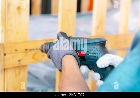 Technician drilling wooden box with drilling machine. Assembly of heavy machinery containers for transport. Technician carpenters wear safety gloves Stock Photo