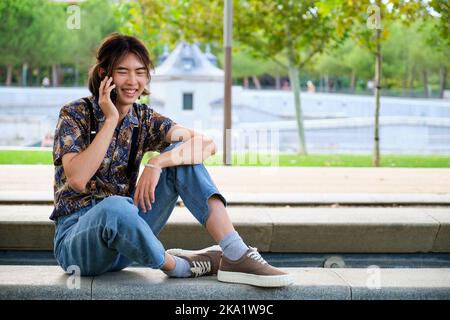 Taiwanese guy smiling and talking on the smartphone at street. Stock Photo