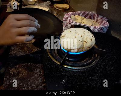 Hands preparing Indian bread, roti or chapati on a gas stove in an Indian kitchen. Dehradun City India. Stock Photo