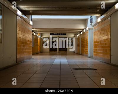 Tunnel interior of the pedestrian underpass between the rail station platforms. Empty undercrossing in a yellow tiled building and doors at the end. Stock Photo