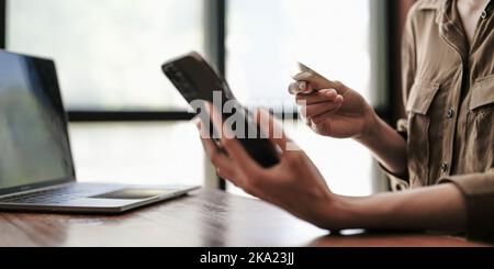Close up female hands holding credit card and smartphone, young woman paying online, using banking service, entering information, shopping, ordering Stock Photo