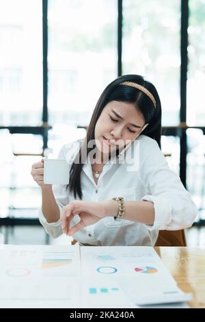 A portrait of a beautiful Asian employee hustle rushing while watch at the clock and talking on the phone Stock Photo