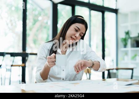 A portrait of a beautiful Asian employee hustle rushing while watch at the clock and talking on the phone Stock Photo