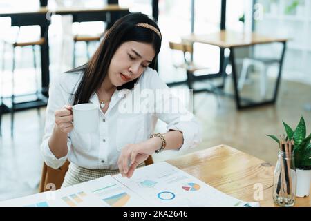 A portrait of a beautiful Asian employee hustle rushing while watch at the clock and talking on the phone Stock Photo