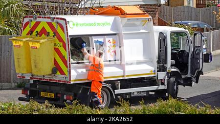 Waste food recycling truck driver high visibility clothing stops to empty household caddy bin into collection lorry residential road Essex England UK Stock Photo