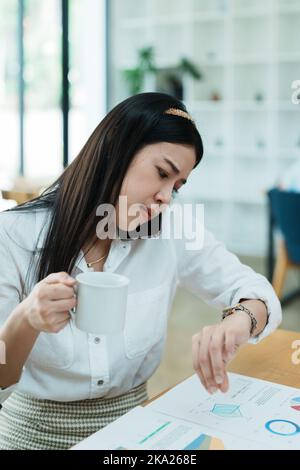 A portrait of a beautiful Asian employee hustle rushing while watch at the clock and talking on the phone Stock Photo