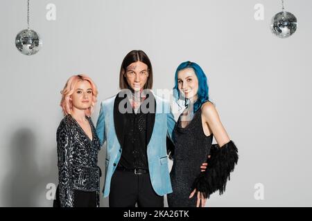 tattooed queer person looking at camera near elegant nonbinary friends smiling at camera on grey background,stock image Stock Photo