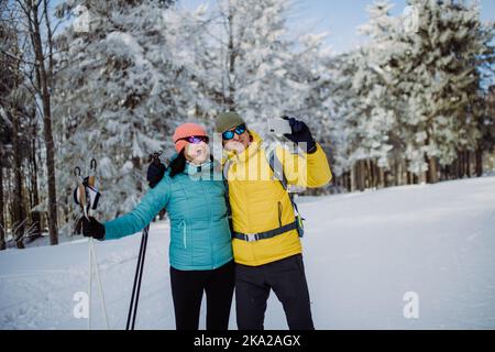 Senior couple taking selfie during cross country skiing in snowy forest. Stock Photo