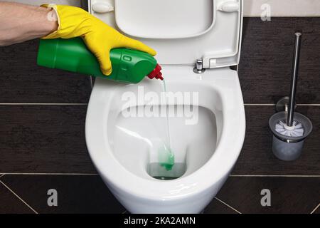 Hands in yellow rubber gloves pour disinfectant into the toilet Stock Photo