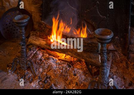 A close up of wood logs burning on a typical hearth fire, with metal fireside ornaments. Stock Photo