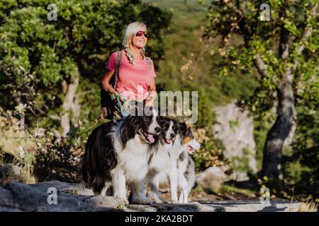 Senior woman walking with her three dogs in forest. Stock Photo