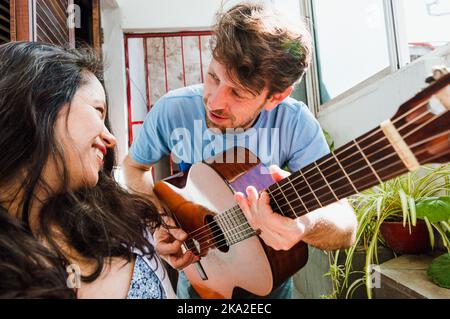 Short-haired Argentine Latin man with a beard very much in love, he sings with his guitar to his wife a young Brazilian woman and who is sitting smili Stock Photo