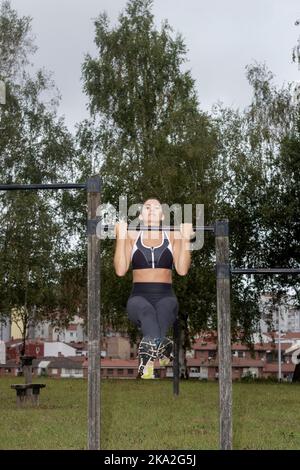 View of a cheerful fit young woman wearing pink sports bra while doing upper body sweep exercise outdoors in a park Stock Photo