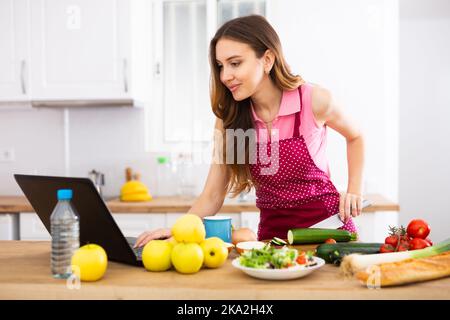 Young housewife using laptop and cooking in home kitchen Stock Photo