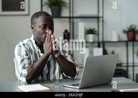 Young troubled African American man keeping hands by his face and looking at lapto pscreen while waiting for web page uploading Stock Photo