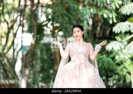 Asian girl in an old rose pink color knee length fluffy dress with high heel slingback shoes and ceremonial thread on her wrist. She is brighter mood Stock Photo