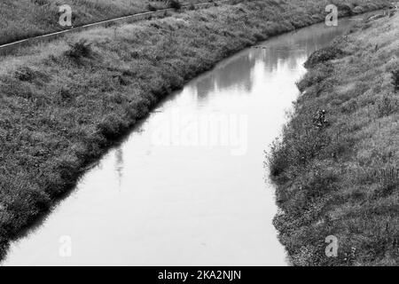 A grayscale shot of a smooth flowing river in a rural field Stock Photo