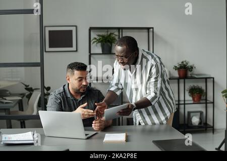 Two young multicultural colleagues with mobile gadgets arguing about online data while preparing presentation together in office Stock Photo