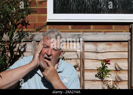 Senior man in pain with toothache. Holding his jaw in agony. Stock Photo