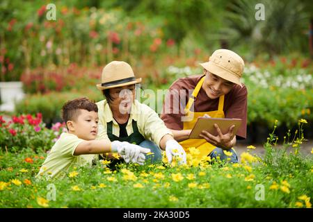 Smiling father taking notes in document on tablet computer when mother and son checking flowers Stock Photo