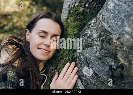 Close up of happy young woman gently touch tree bark covered in green lush moss at autumn day. Forest conservation, saving environment, green movement Stock Photo