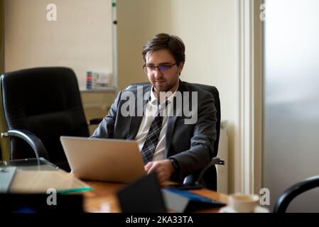 Young serious  professional business man, focused male student wearing glasses working on laptop Stock Photo