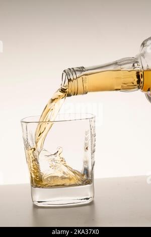 pour whiskey or bourbon into a glass on a beige white background vertical studio shot. Stock Photo