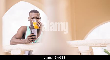African American man drinking juice and using cellphone Stock Photo