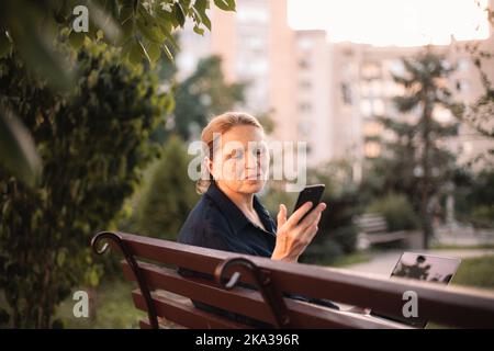 Happy mature business woman using smart phone and laptop in park Stock Photo