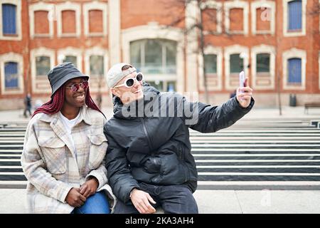 multiethnic couple using phone taking selfie, on the street Stock Photo