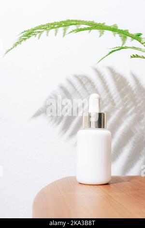 White serum bottle on a background of white wall with fern leaf shadow. Natural skincare products concept. Stock Photo