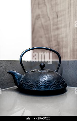 Traditional teapot on table of zen minimalist home with wooden wall background and vertical closeup view of cast iron tea teaware Stock Photo