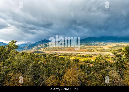 Wide angle view of Aspen, Colorado Rocky mountains at storm stormy sunset with cloudy clouds sky of blue skyscape by oak trees in foreground Stock Photo