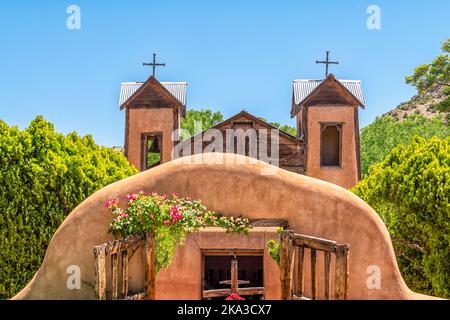 Famous historic adobe El Santuario de Chimayo sanctuary church in the United States with entrance gate closeup of flowers in summer Stock Photo