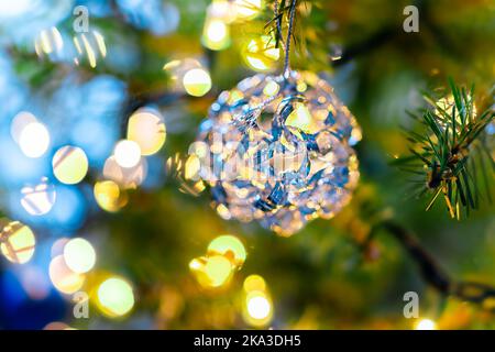 Macro closeup of colorful blue yellow decorative ornament hanging on New Year Christmas tree with light illuminations in winter with bokeh circles in Stock Photo