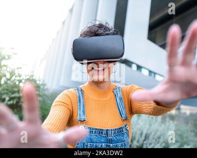 Cheerful woman in VR goggles interacting with virtual reality while playing video game on sunny day Stock Photo