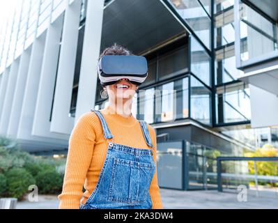 Cheerful woman in VR goggles interacting with virtual reality while playing video game on sunny day Stock Photo