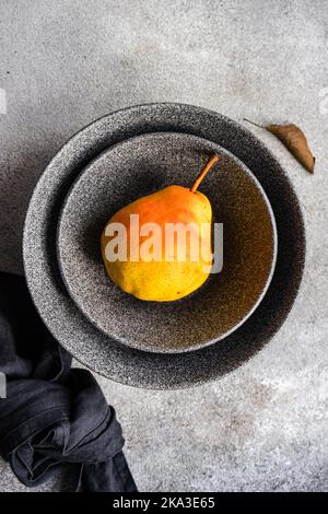 From above ceramic bowl with organic pears fruit on concrete surface Stock Photo